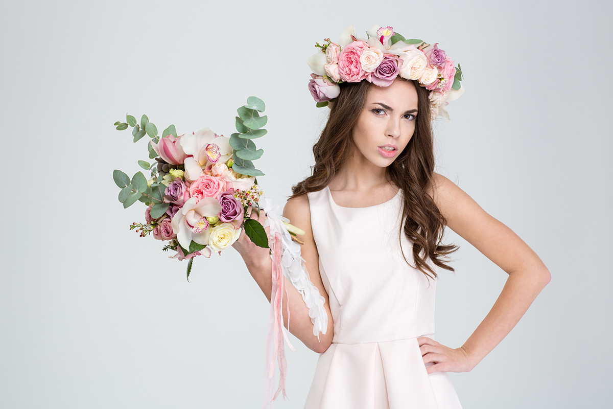 Attractive irritated woman in rose wreath showing bouquet of flowers